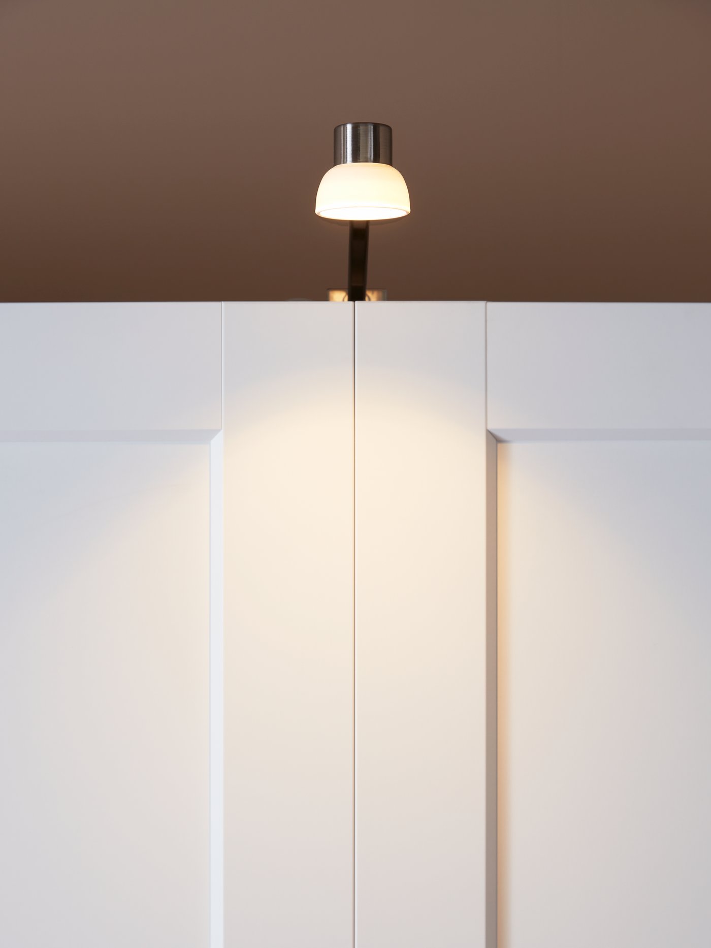 Lampu kabinet LED LINDSHULT dilekapkan di bahagian atas almari pakaian, memancarkan cahaya pada pintu almari pakaian yang tertutup.