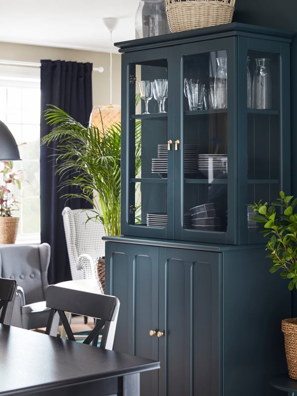 Mobile LOMMARP blu scuro-verde con ante a vetro accanto a un tavolo da pranzo, con stoviglie a vista - IKEA