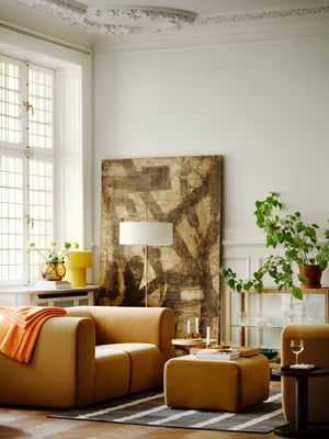 A living room with a beige STOCKHOLM 2025 2-seat sofa as the centrepiece, a matching pouffe, a table lamp, and side tables.