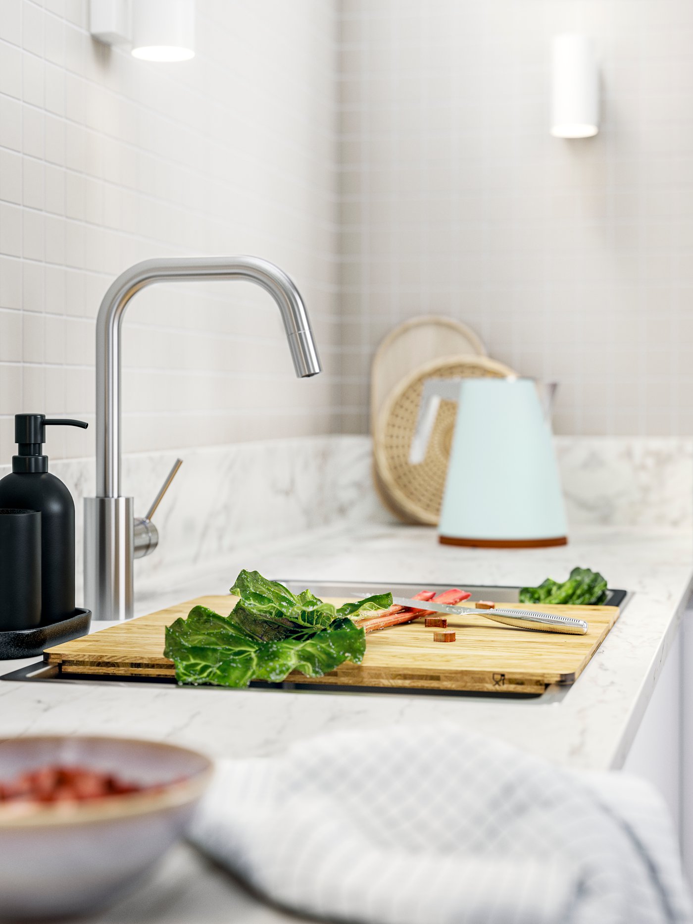 En köksbänkskiva med en NORRSJÖN skärbräda, färska grönsaker och en vattenkokare, allt mot ett kaklat stänkskydd.