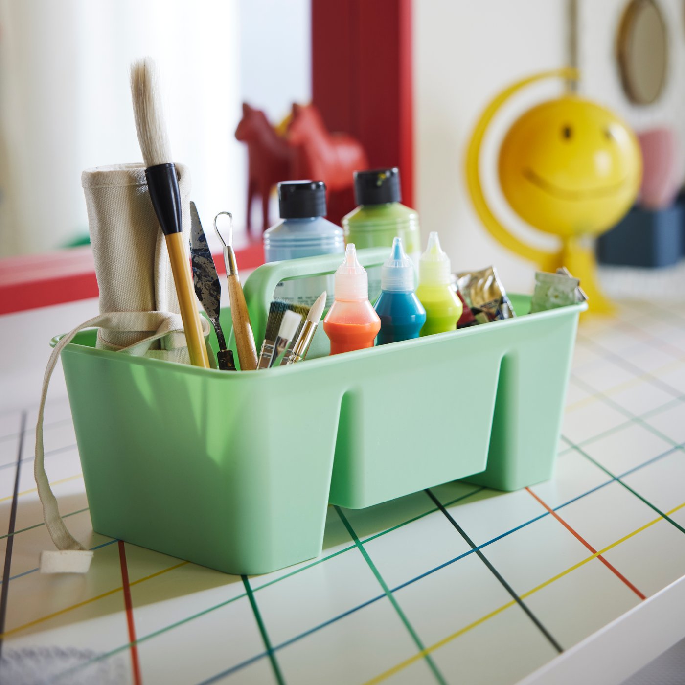 The green STACKSTOD desk organiser holding paint colours and brushes, placed on a colourful desk.