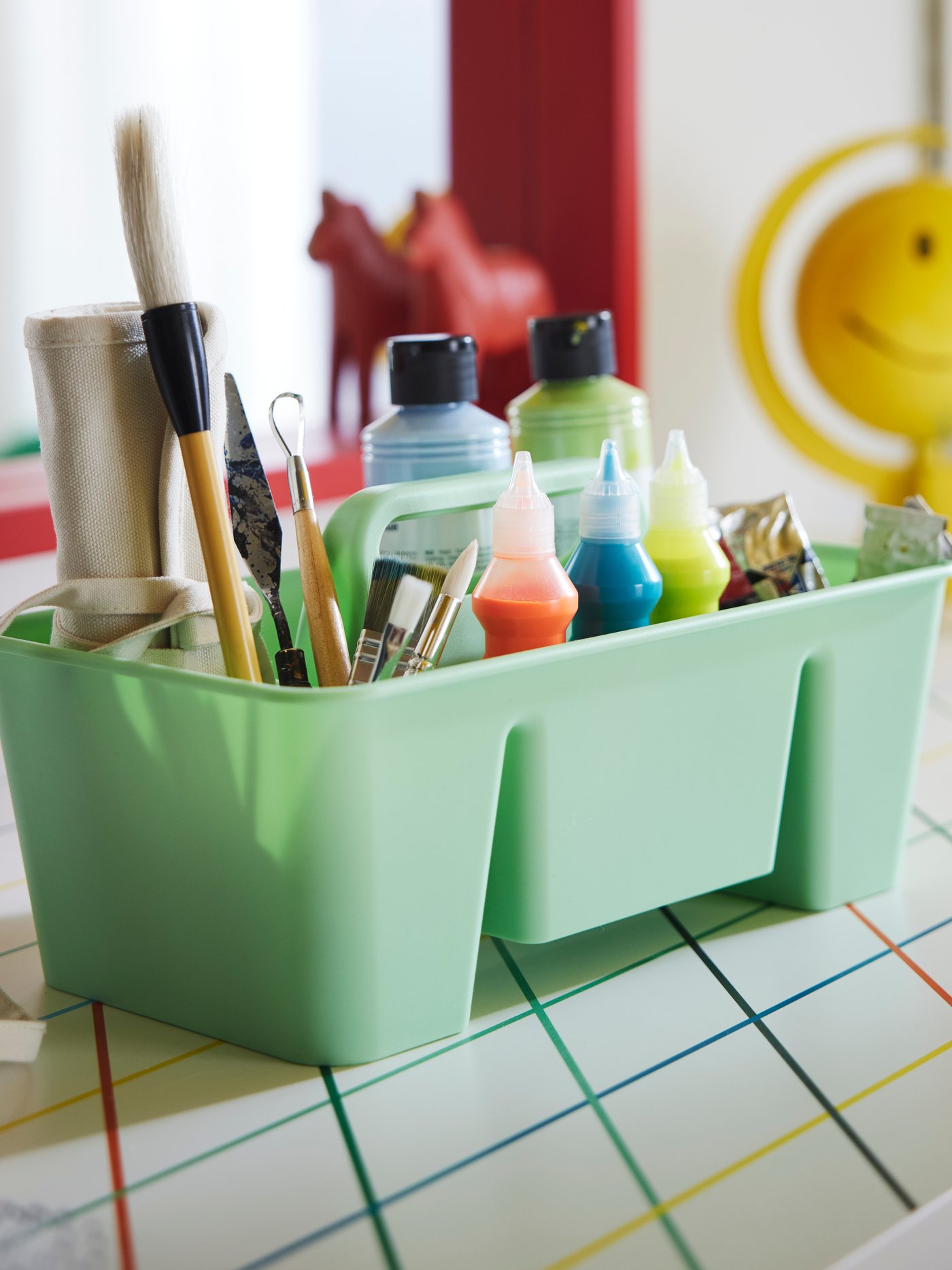The green STACKSTOD desk organiser holding paint colours and brushes, placed on a colourful desk.