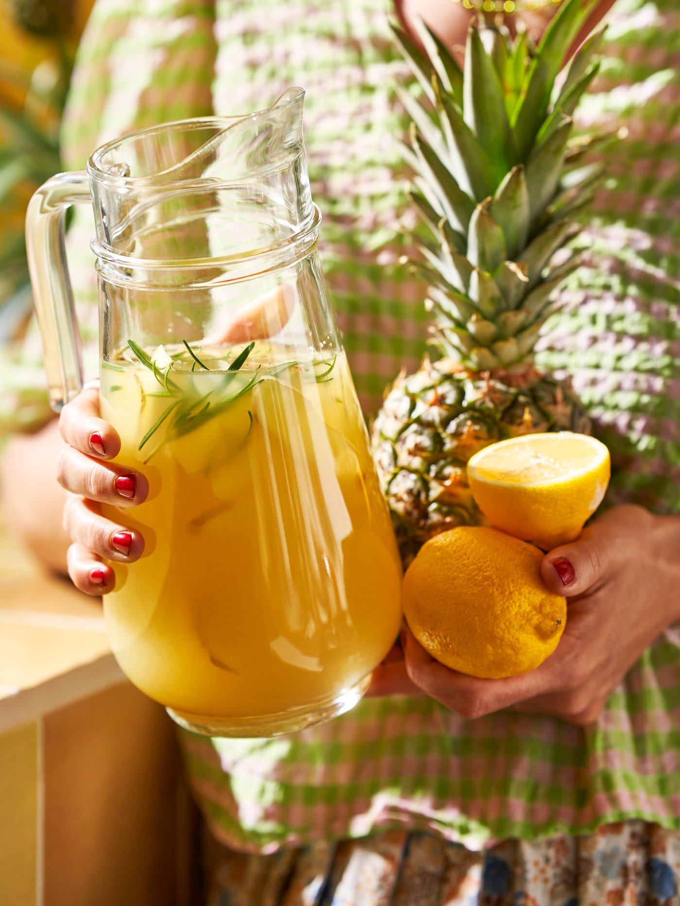 Una persona sostiene una jarra de vidrio incoloro TILLBRINGARE llena de zumo y frutas, en una cocina.