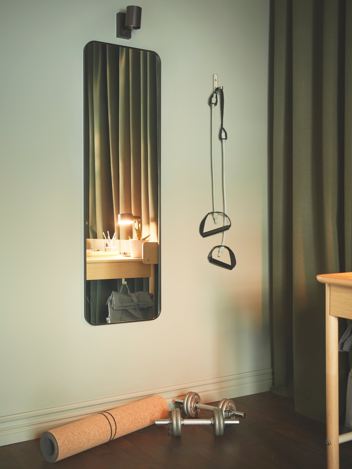A green-colour-scheme room with minimalistic gym accessories collected by a black LINDBYN mirror beneath a NYMÅNE lamp.