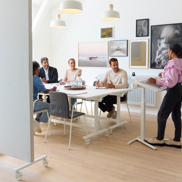 A long shot of people sitting at a white table in a meeting room.
