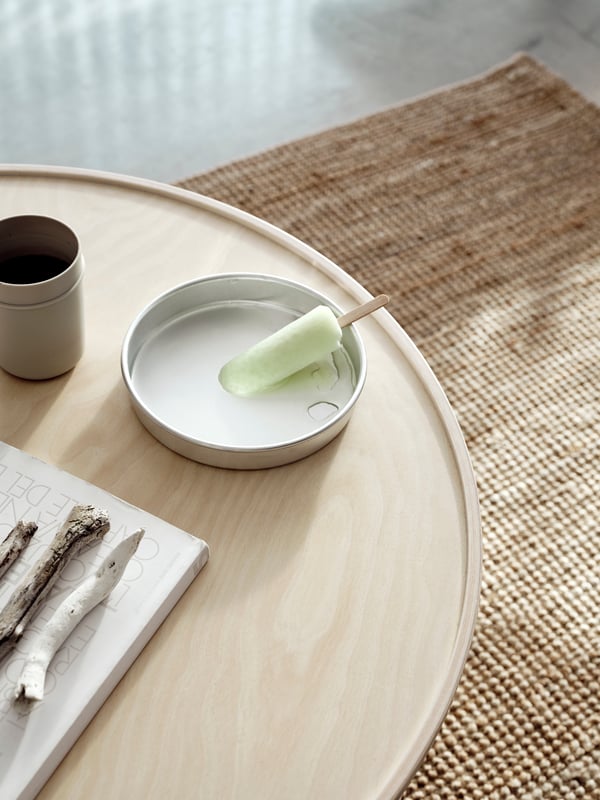 An ice lolly melts in a dish on the BORGEBY coffee table, with birch veneer surface and edged lip in focus.