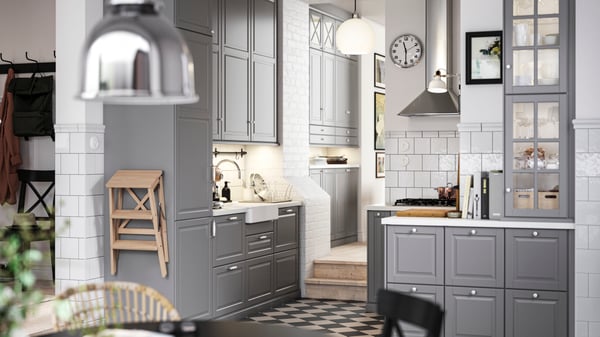 A traditional kitchen with a chequered floor, grey BODBYN kitchen fronts and white/light grey stone effect/laminate worktops.