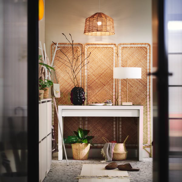 A hallway with a rattan TOLKNING room divider flat against a wall at the end with a white MALM dressing table in front of it.