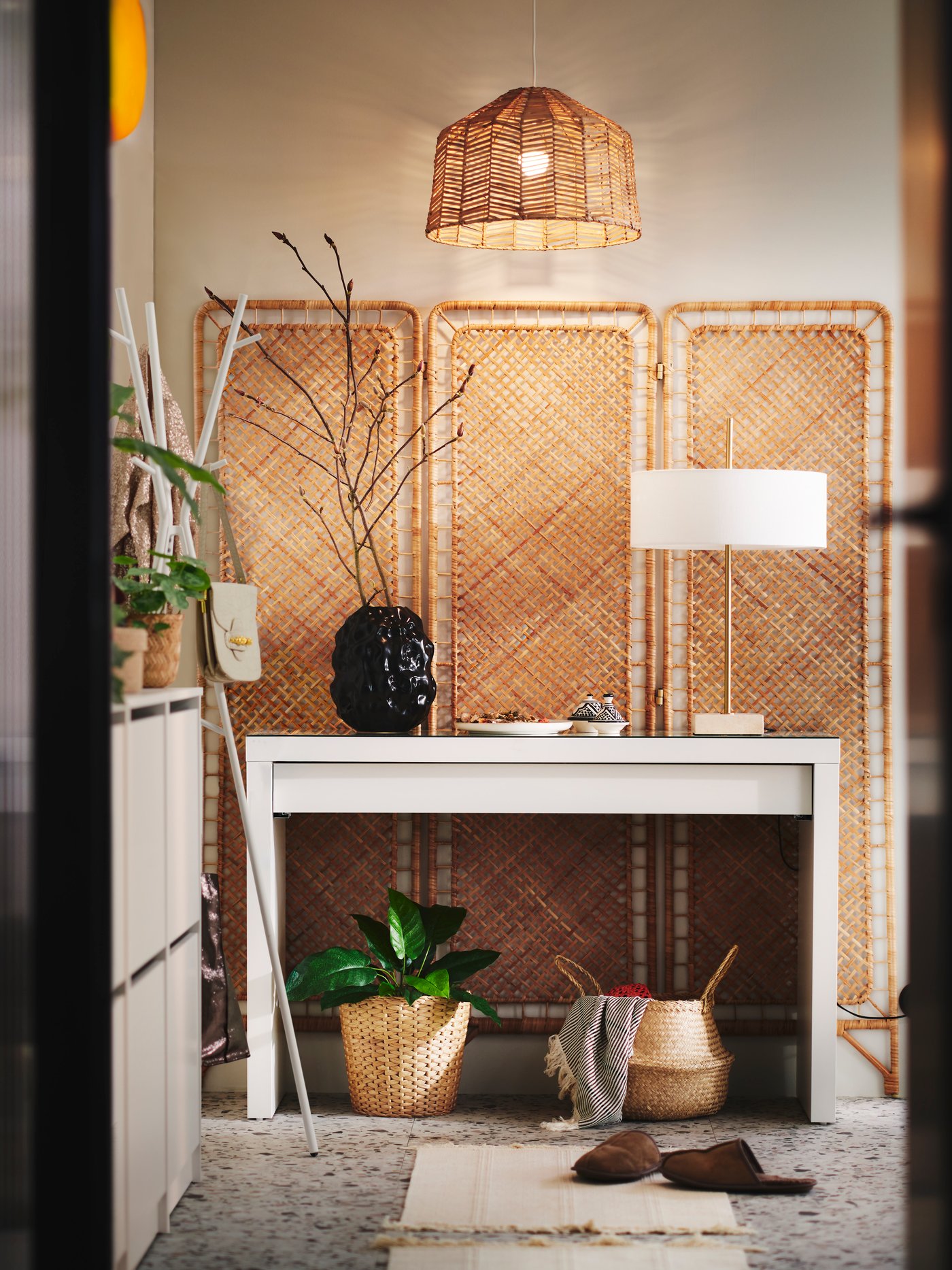 A hallway with a rattan TOLKNING room divider flat against a wall at the end with a white MALM dressing table in front of it.