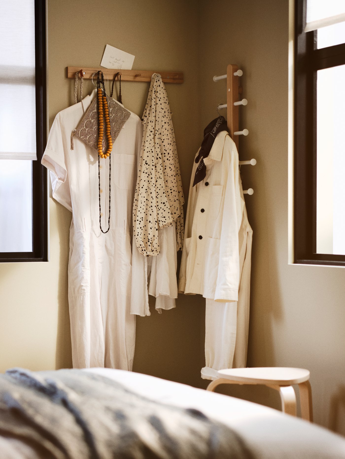 Un gancho HÖVOLM y otro colgador puestos en la pared con prendas colgadas.