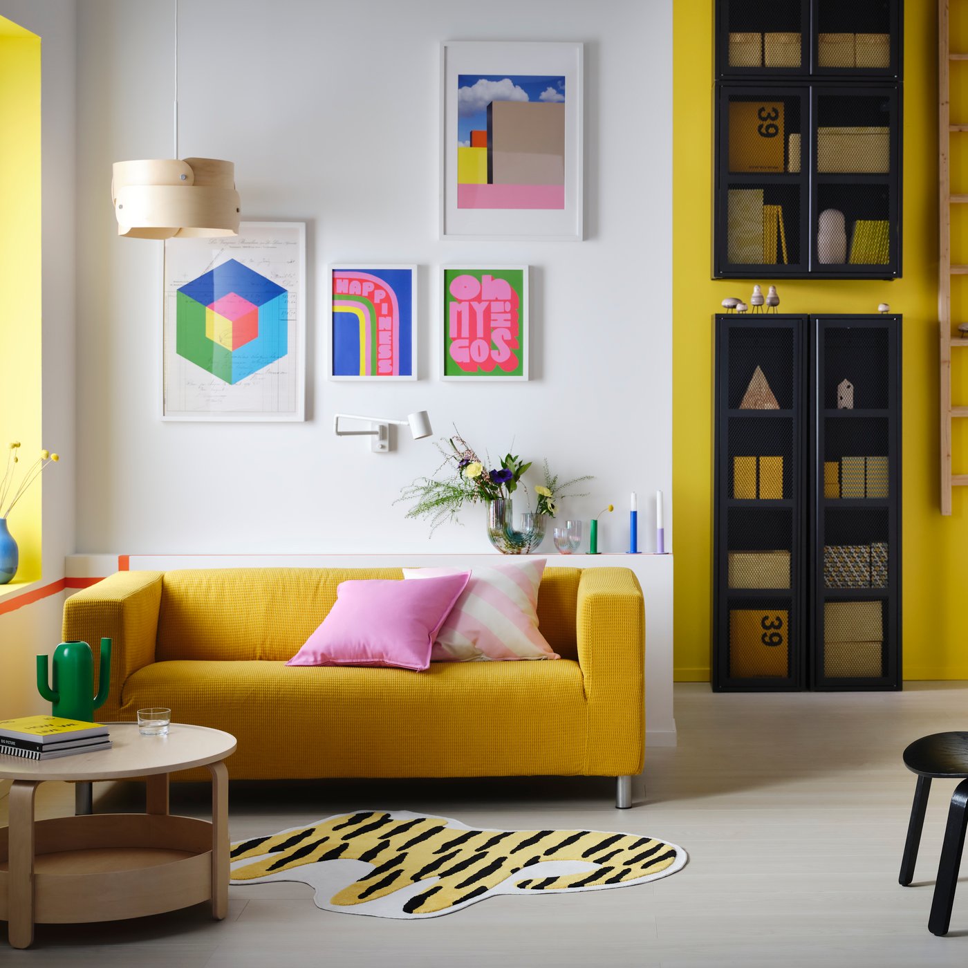 A Scandinavian living room with a yellow sofa, pink cushions and colourful posters on the wall. On the floor lies a tiger-shaped rug.