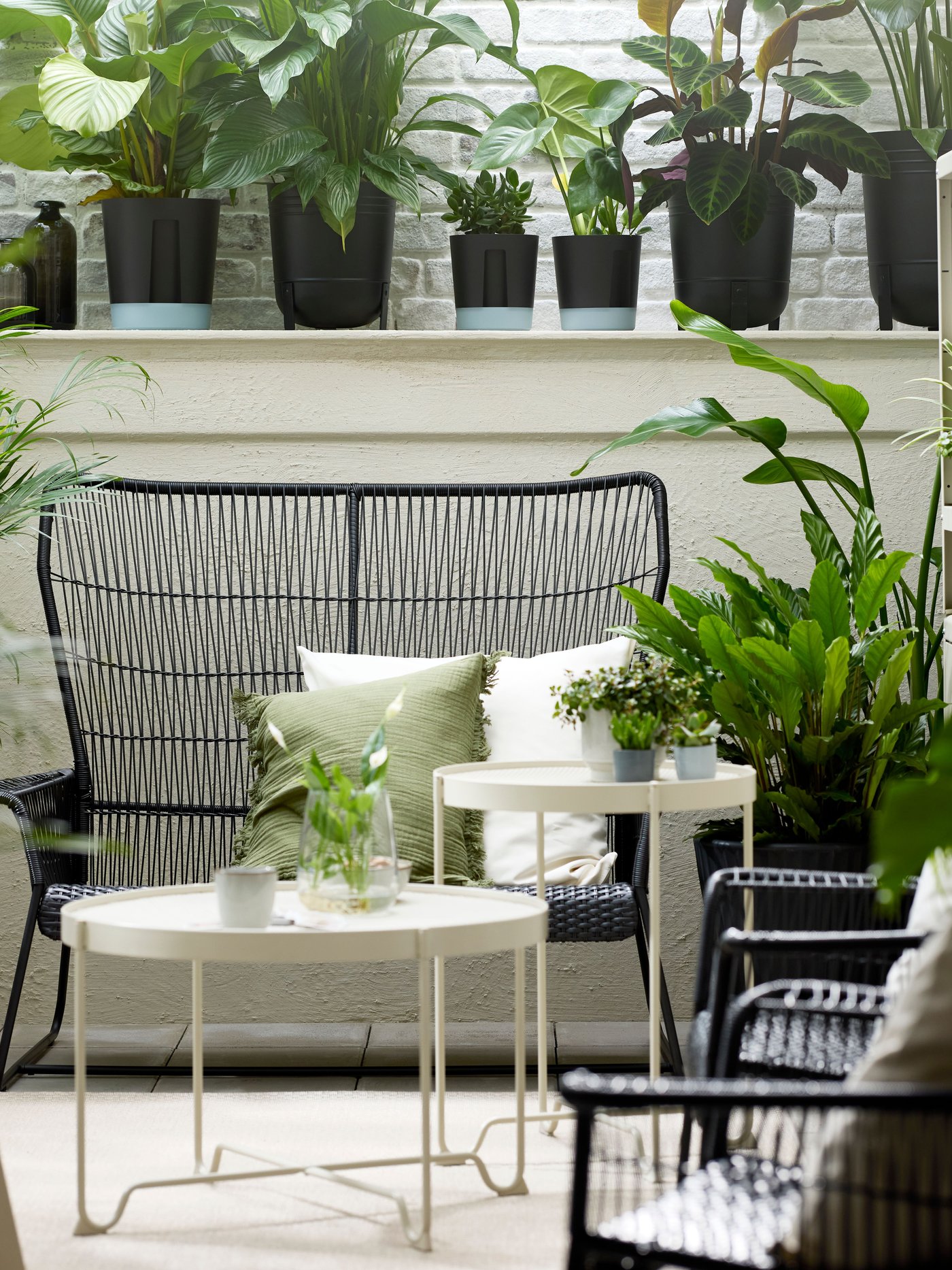 Une véranda avec des plantes vertes et un canapé d'extérieur 2 places TALLSKÄR, avec une table d'appoint KROKHOLMEN et une table basse au milieu.