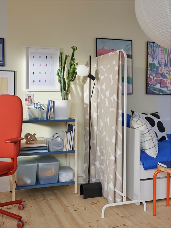 An EKENABBEN open shelving unit with storage accessories next to a black floor lamp and a clothes rack with a draped fabric.