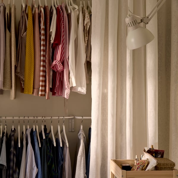 A storage solution with clothes hanging on rods at two different heights, with a white curtain half open in front of it.