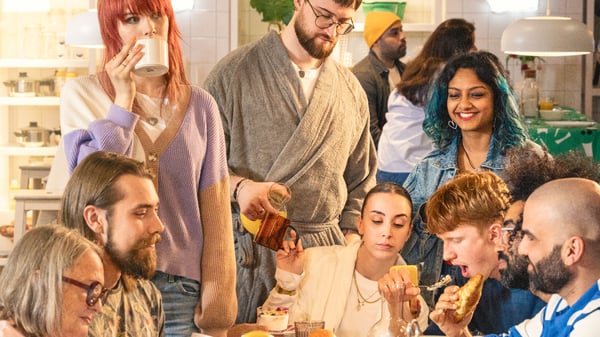 Grupa veselih ljudi uživa u doručku u izložbenom prostoru u robnoj kući IKEA.