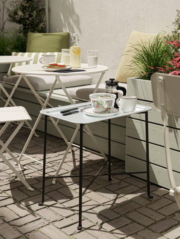 A tray table with a light blue tray and black legs with a bowl of salad, coffee and cutlery on it.