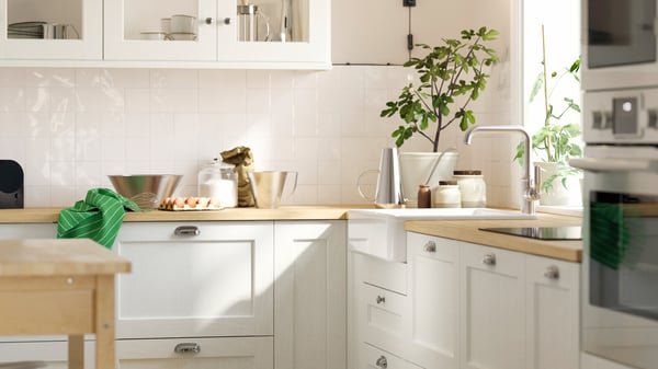 白いイケアのキッチン収納と木製カウンター、シンク、植物、卵や調理器具がある明るいキッチン。