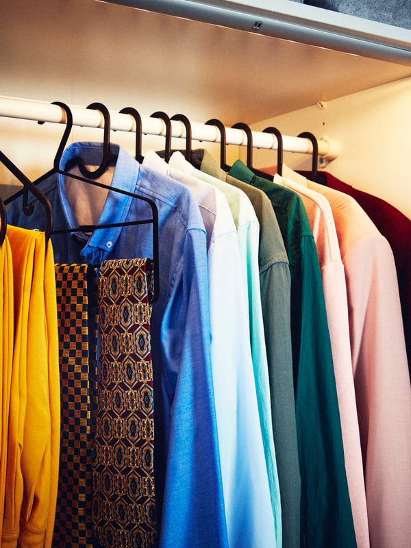 Close-up of wardrobe with light orange interior, multiple trouser hangers on a rail, multiple shirts and ties.