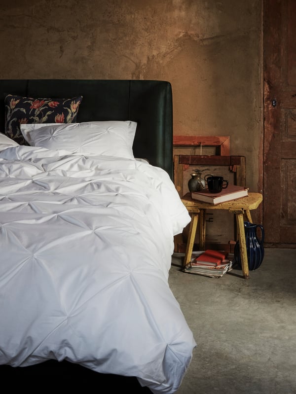 Rustikales Schlafzimmer mit weißer Bettdecke und dunklem Kopfteil neben einem kleinen Holztisch mit Teekanne und Büchern