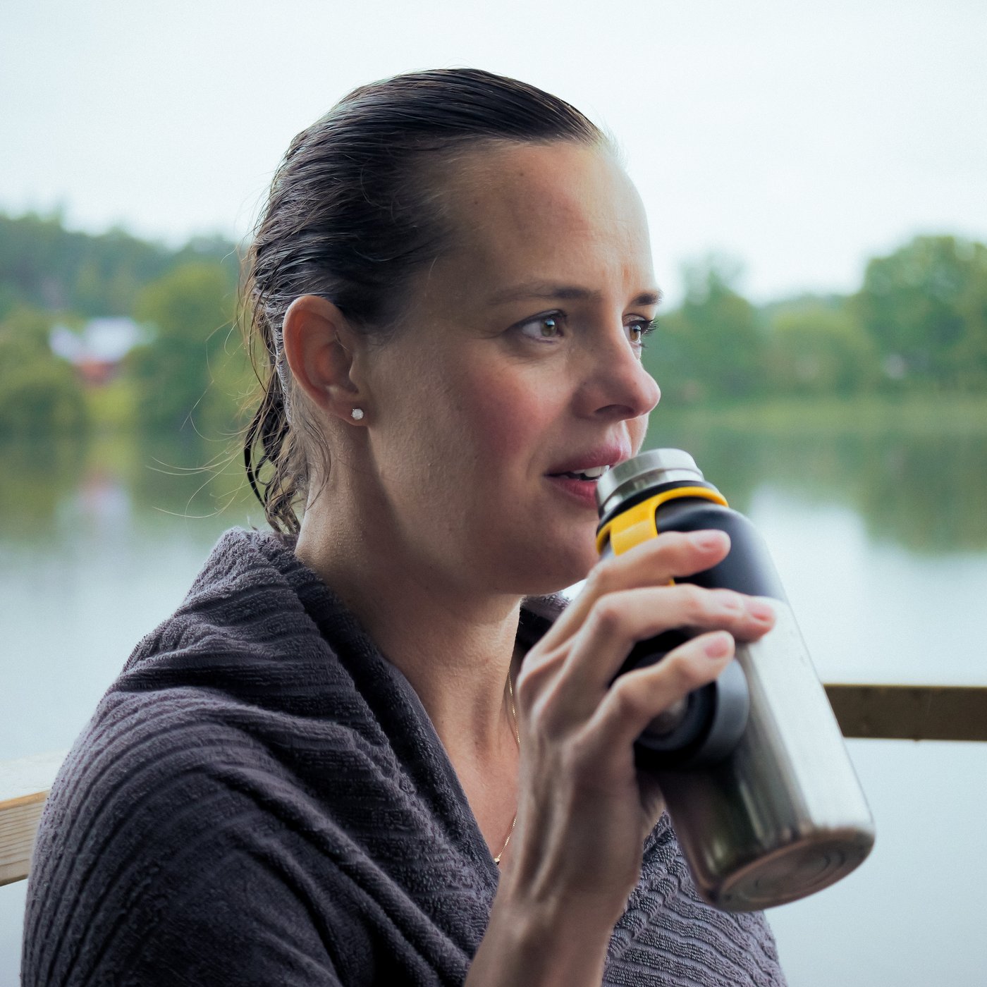 Una donna seduta vicino a un lago beve una bevanda calda da un contenitore termoisolato HETLEVRAD.