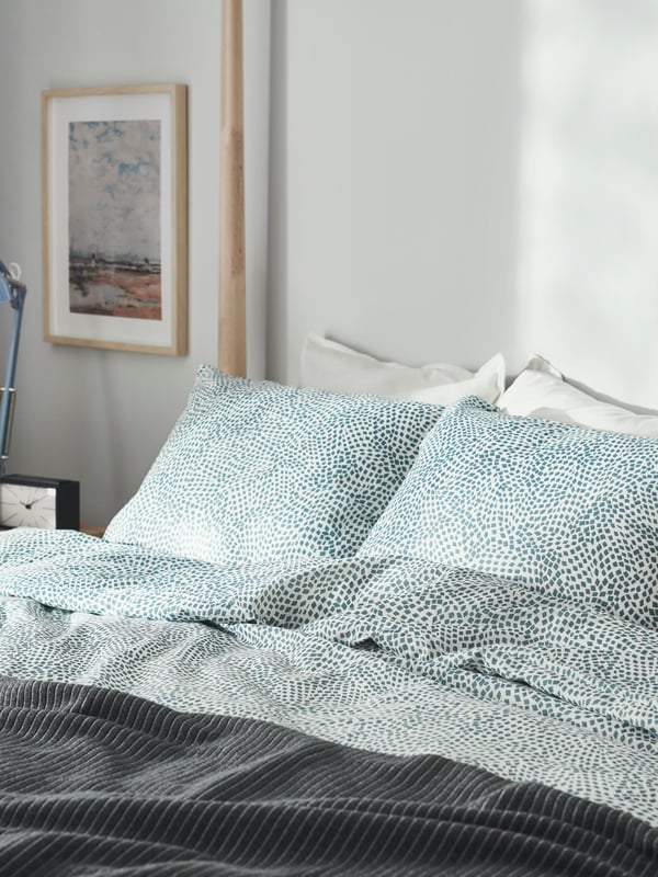 Ein Bett mit blau weiß gepunkteter Bettwäsche. Darüber liegt eine graue Tagesdecke.