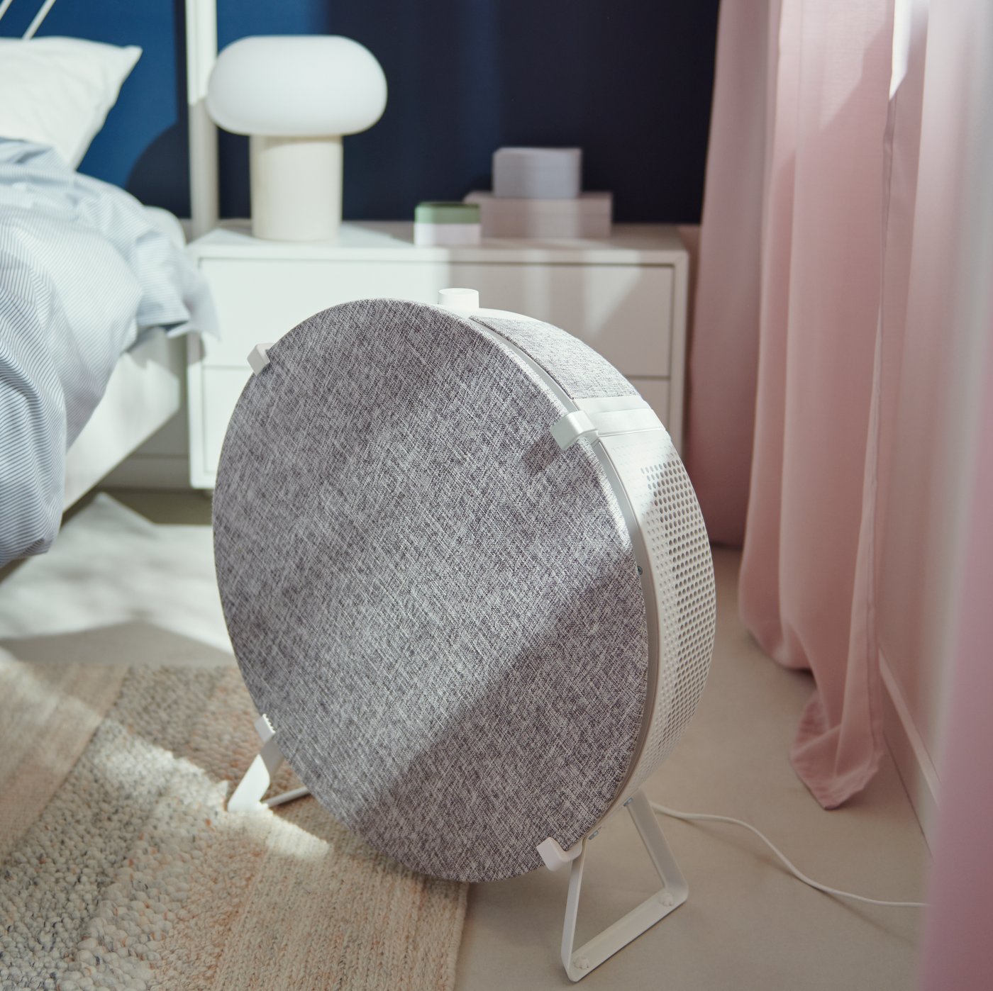 Ein IKEA STARKVIND Luftreiniger steht auf dem Boden neben einem Bett. 