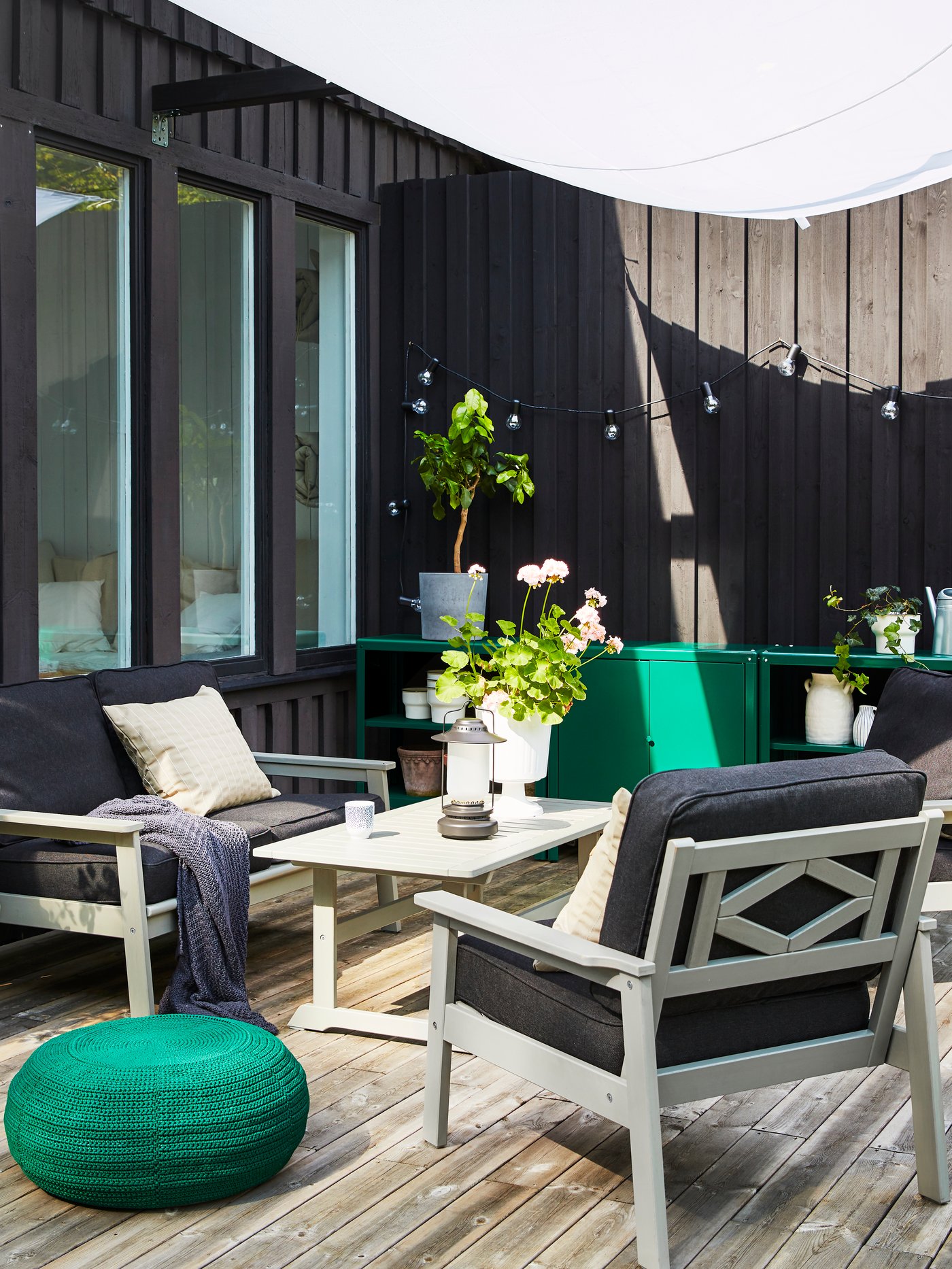 An outdoor space with BONDHOLMEN sofa, armchairs and a coffee table in grey. Beside them is a round, dark green pouffe.