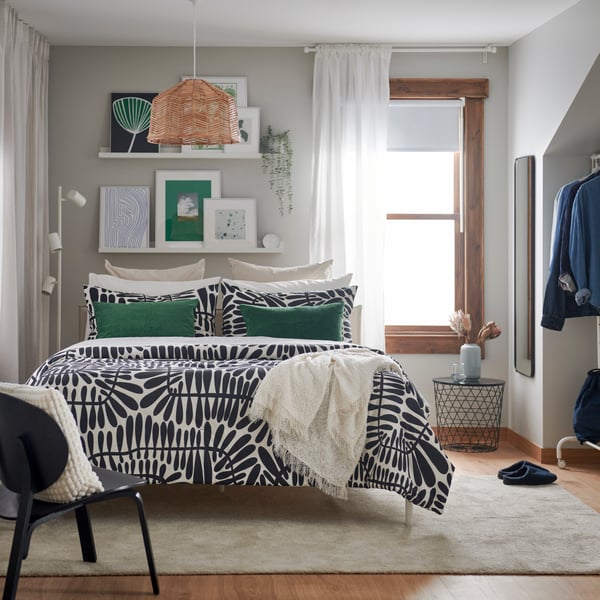 A earthy styled bedroom with a black and white comforter and green, cream and white pillows on a bed.