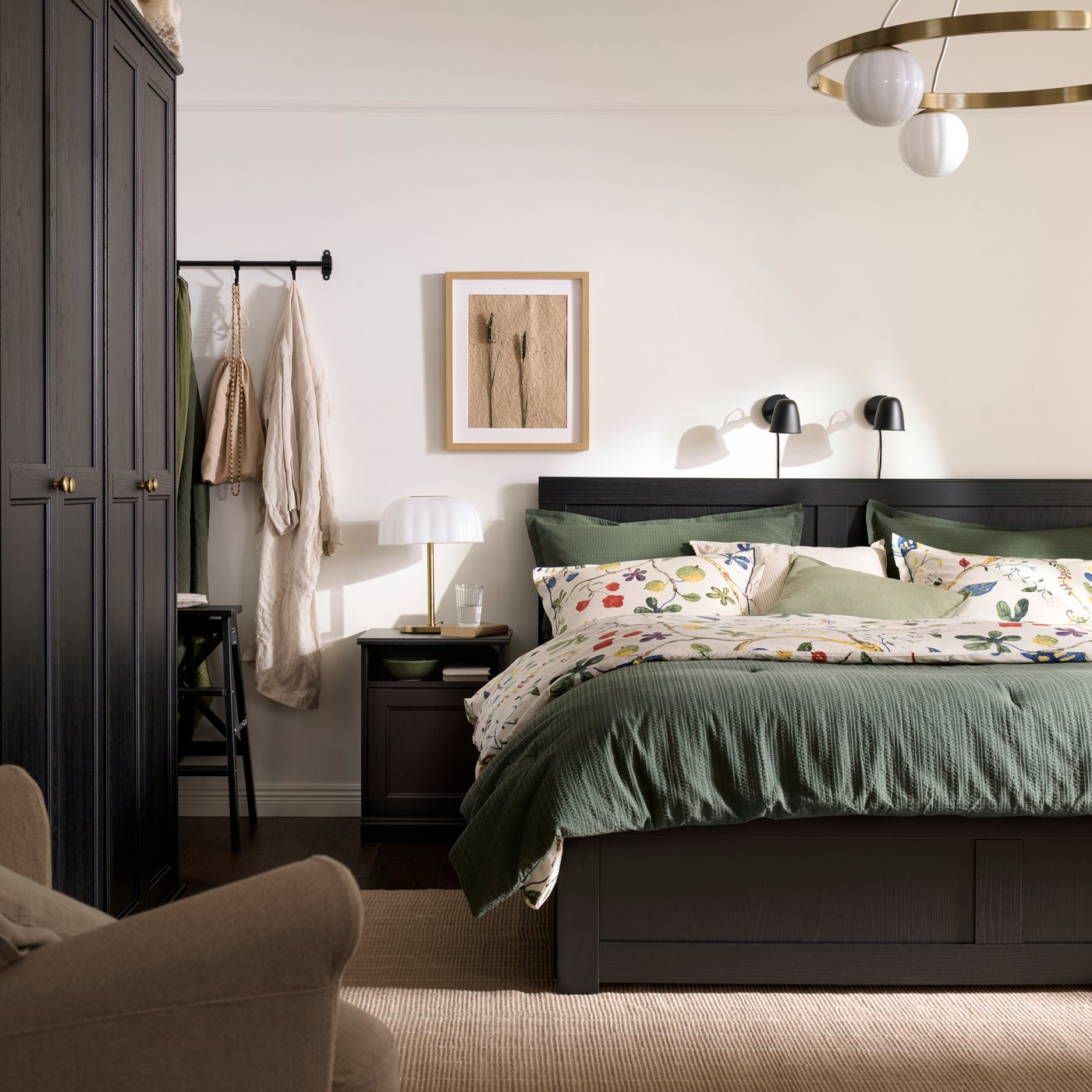 A traditional-style bedroom with a black FÅGELFJÄLLET bed, bedside table and wardrobe and green and floral bedding.