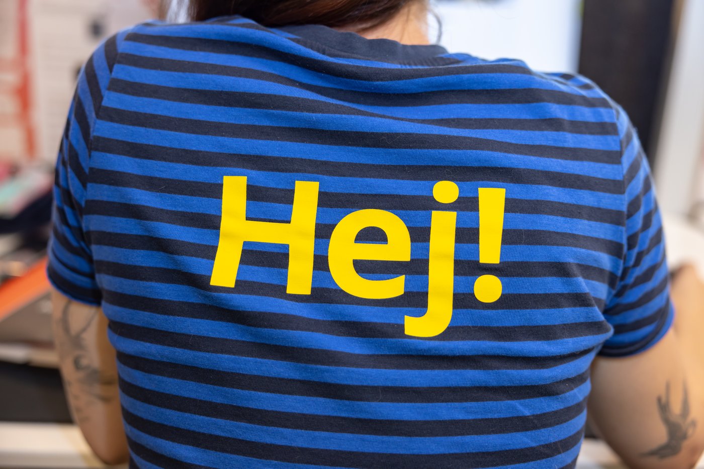 Collaboratrice IKEA de dos avec "Hej!", bonjour en Suédois d'écrit dans le dos