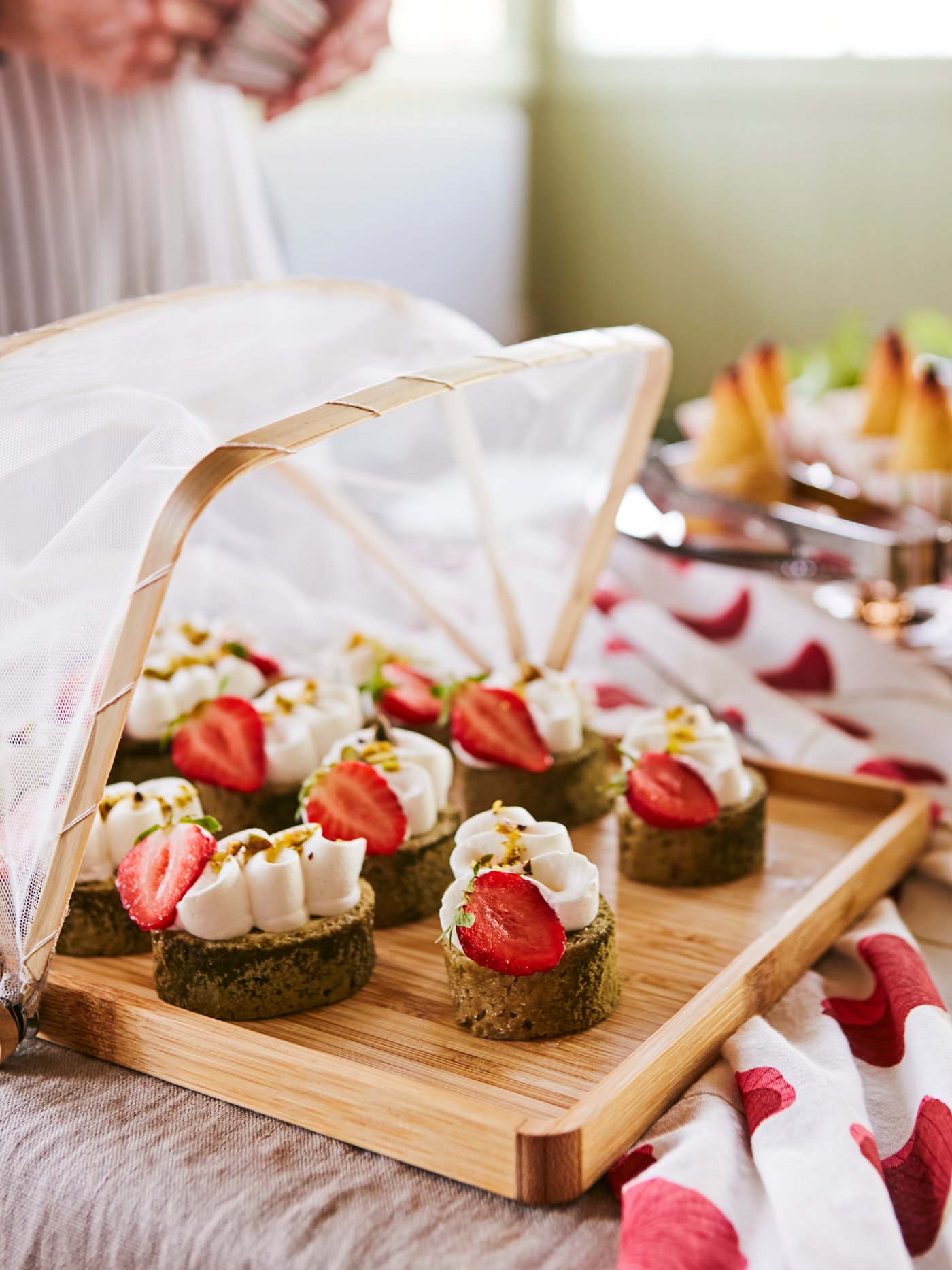 ANLEDNING tray with an insect net holding different canapés with cream and strawberries, placed on a party table.