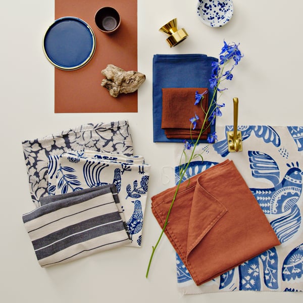 Een staal van BITTERSÖTA voorgesneden stof in beige en blauw, tentoongesteld naast diverse decoratieve artikelen en textiel.