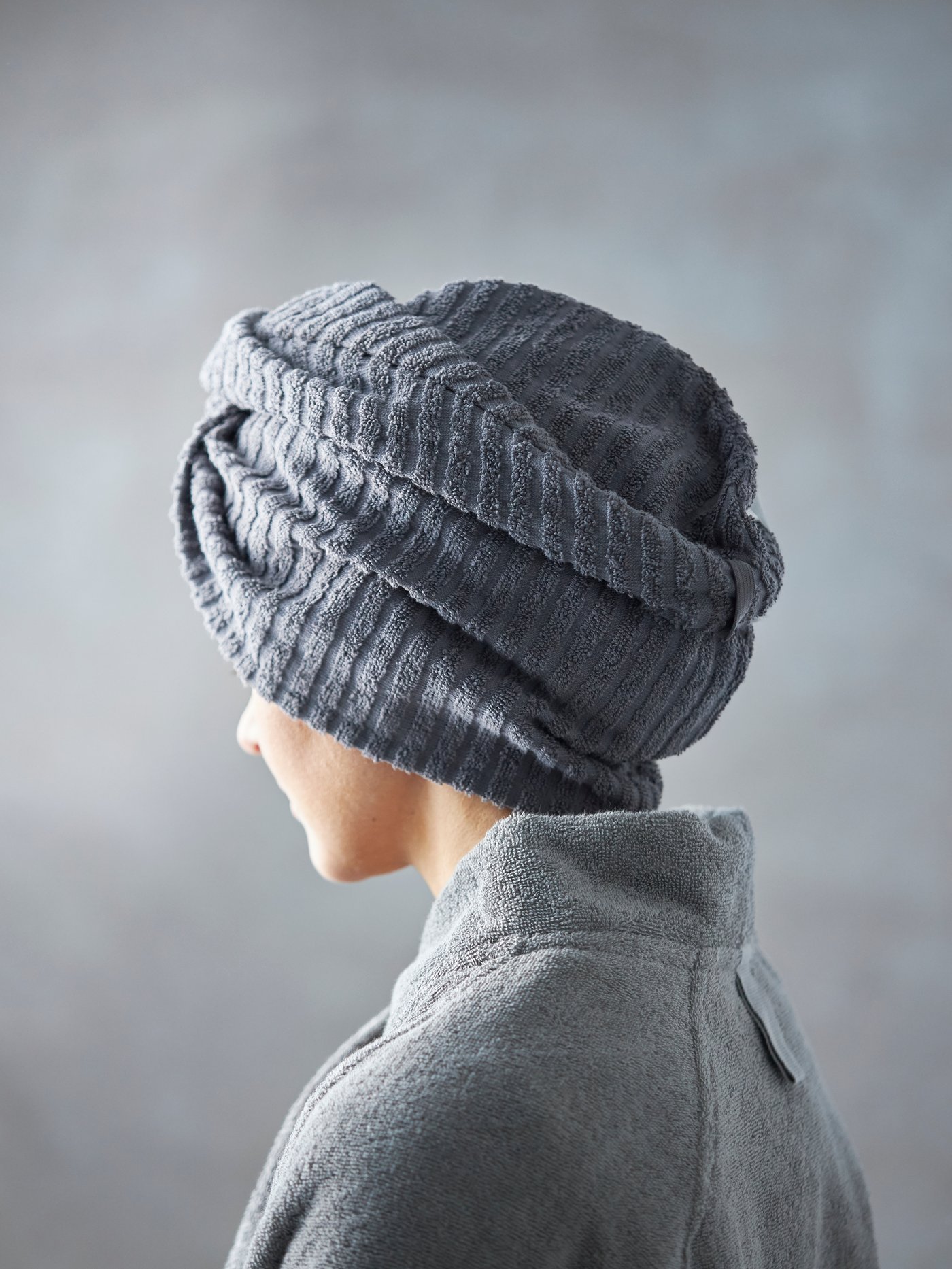 The upper part of the face of a woman standing in a green-tiled bathroom with a blue MÅLSELVA towel wrapped around her head.