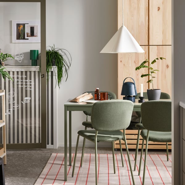 VIHALS chairs stand at a green VIHALS extendable table on a rug underneath a white ZEBRASÄV pendant lamp in a dining room.