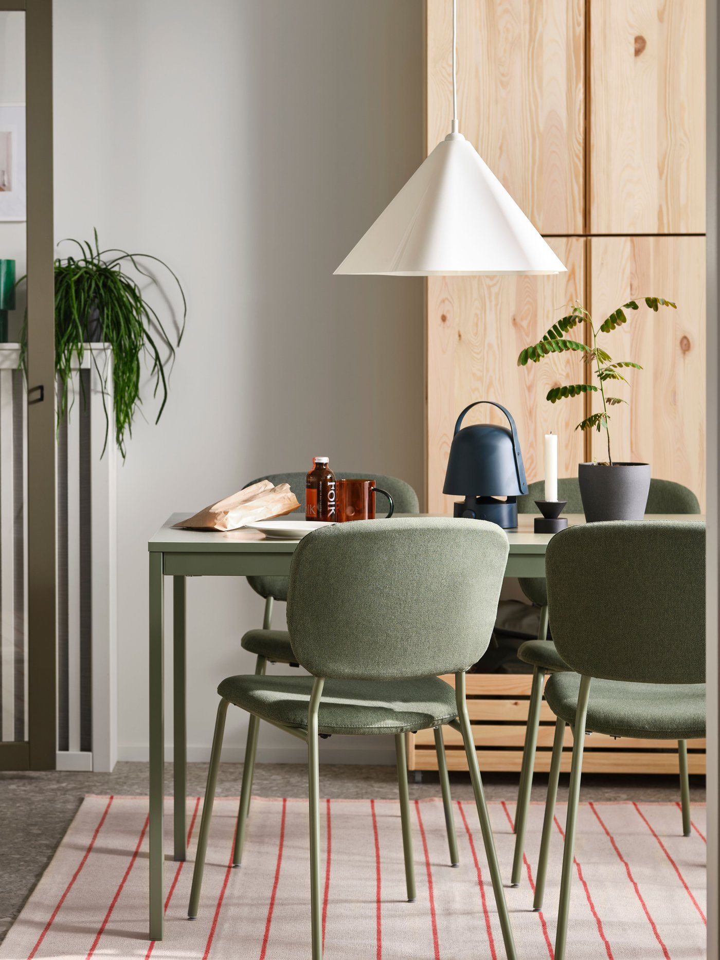 Dans une salle à manger, chaises VIHALS autour d’une table à rallonge VIHALS verte sur un tapis, sous une suspension ZEBRASÄV blanche.