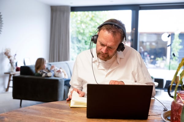 Un homme travaille avec un casque sur son pc avec un enfant à l'arrière sur un canapé
