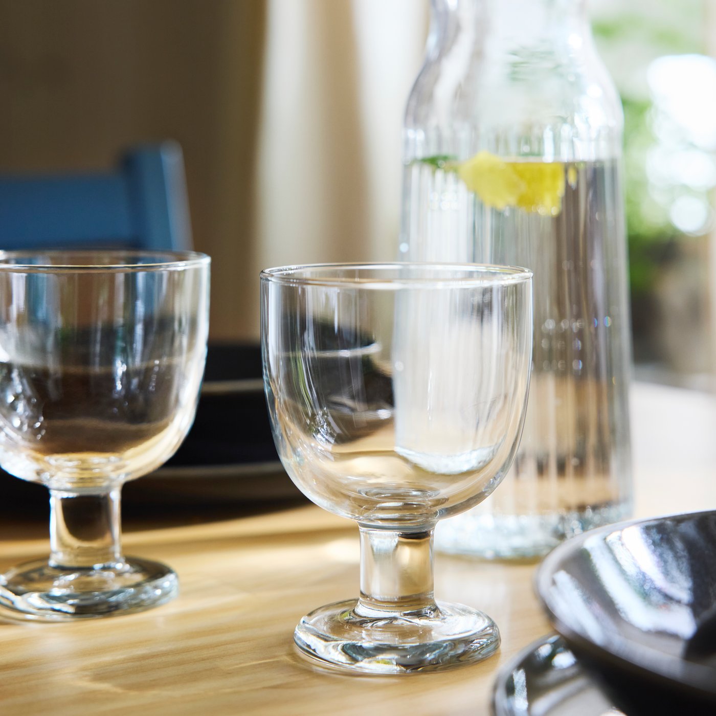 Two FRUKTDUVA goblets stand on a table in front of a VARDAGEN carafe containing water and a slice of lemon.