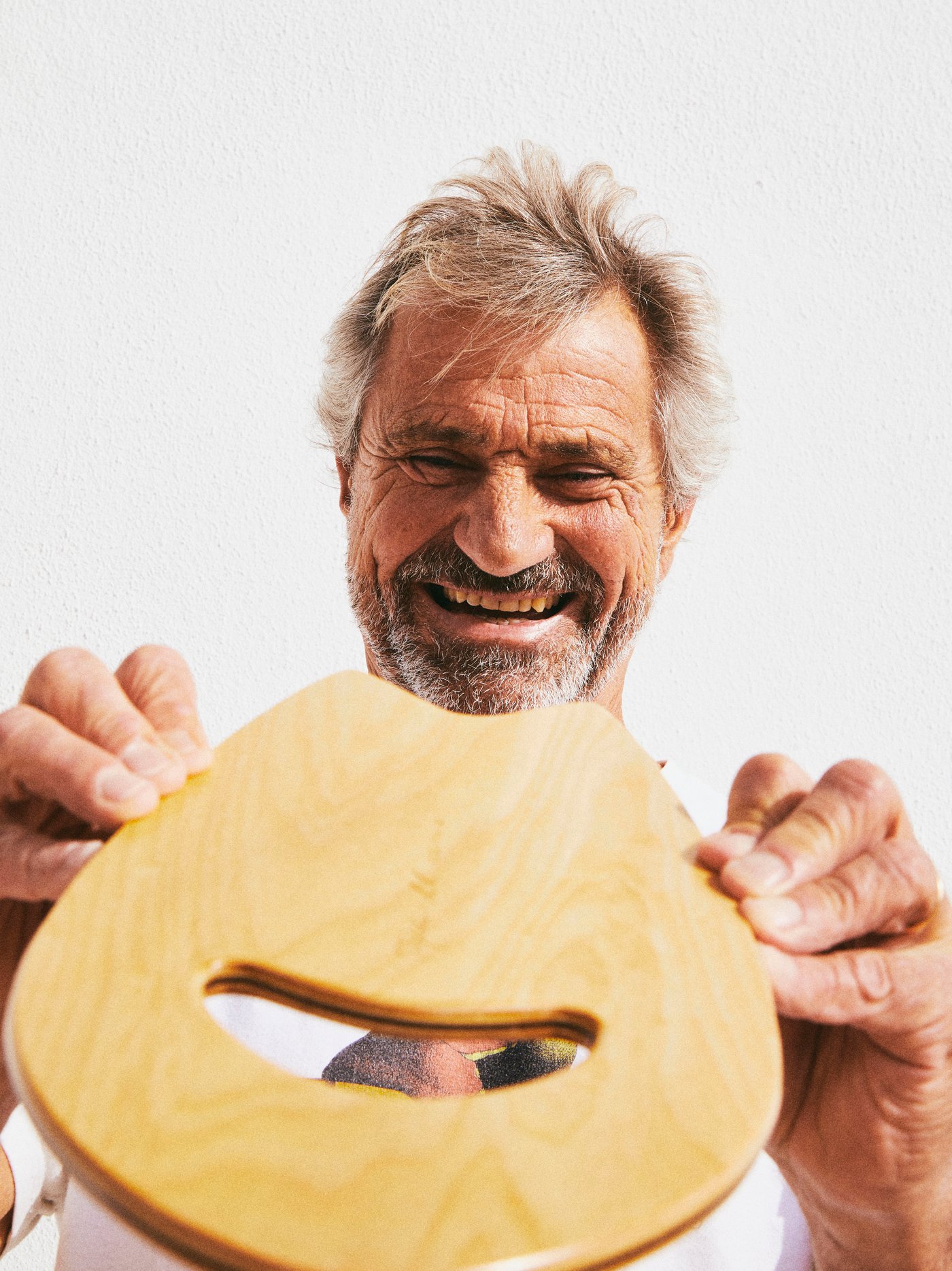 한 남성이 손을 넣을 수 있는 구멍이 뚫려 있는 목재 KÅSEBERGA 코세베리아 핸드플레인을 양손으로 들고 기뻐하는 모습.