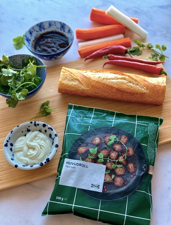 A selection of ingredients for a meal: fresh herbs, sauces, chillies, carrots, a baguette and a ready meal on a wooden board.