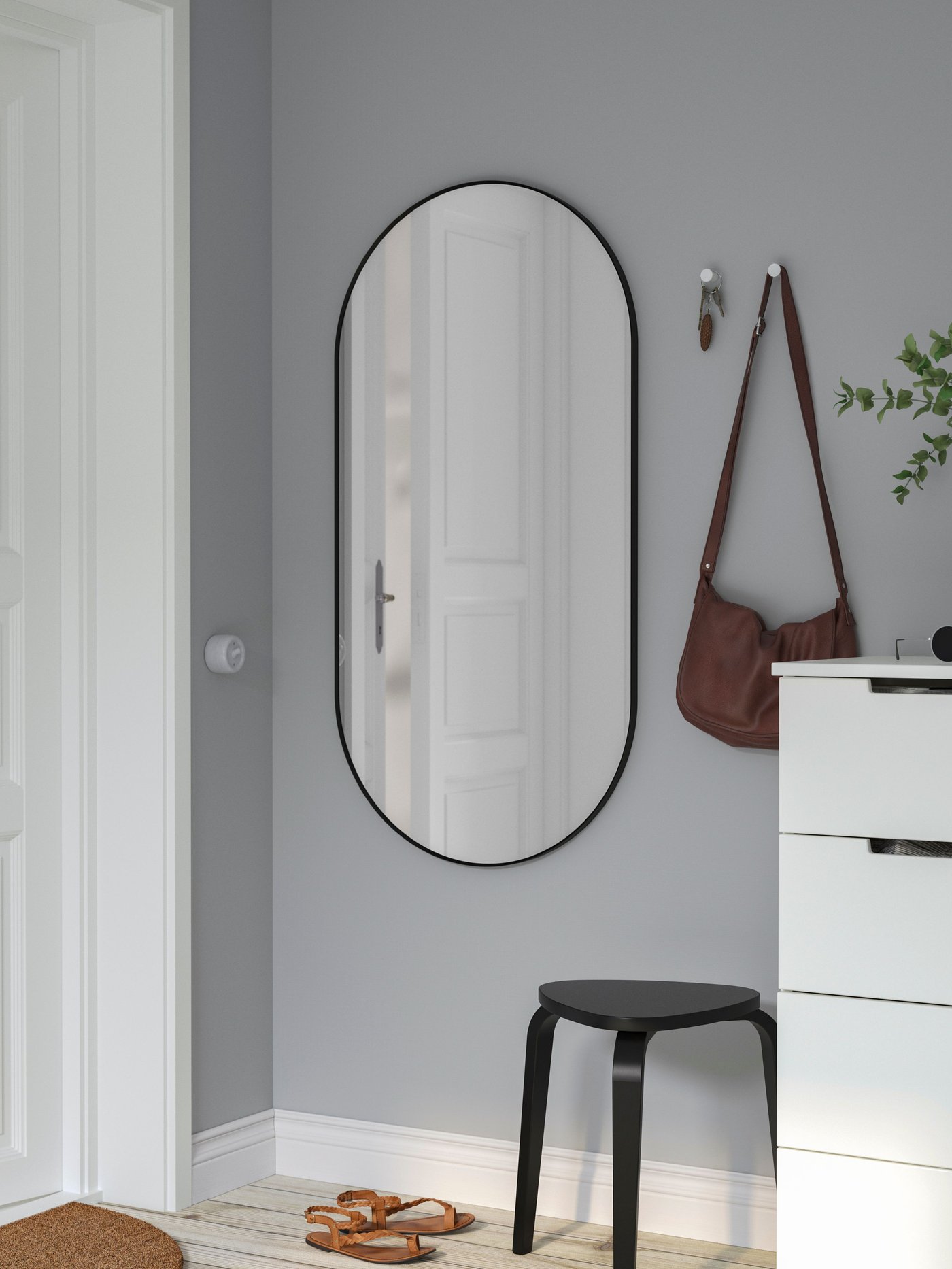 Soikea, musta kehyksinen LINDBYN-peili valoisan eteisen seinällä.