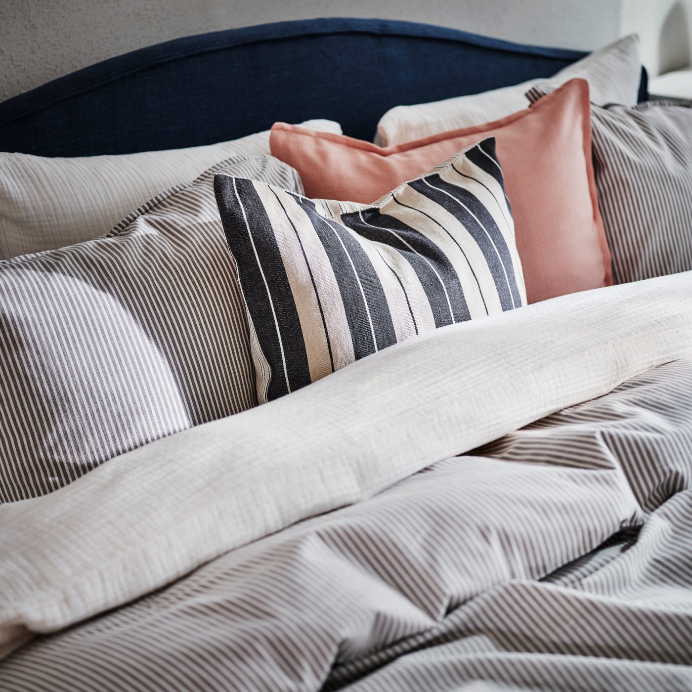 The top of a RAMNEFJÄLL bed covered in SCHERSMIN and SOLFIBBLA bed linen and cushions in LAGERPOPPEL and KORALLBUSKE covers.