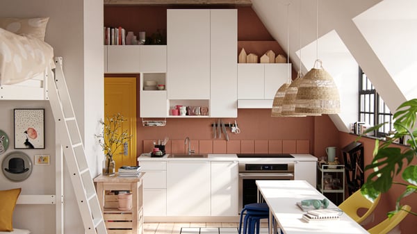 A studio apartment with large industrial-style windows, dark terracotta-coloured walls and white VALLSTENA kitchen fronts