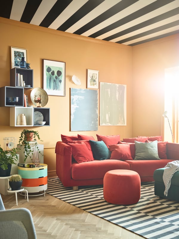 Gemütliches Wohnzimmer mit rotem 3er-Sofa, gestreiftem Teppich und moderner Dekoration in warmen Erdtönen.