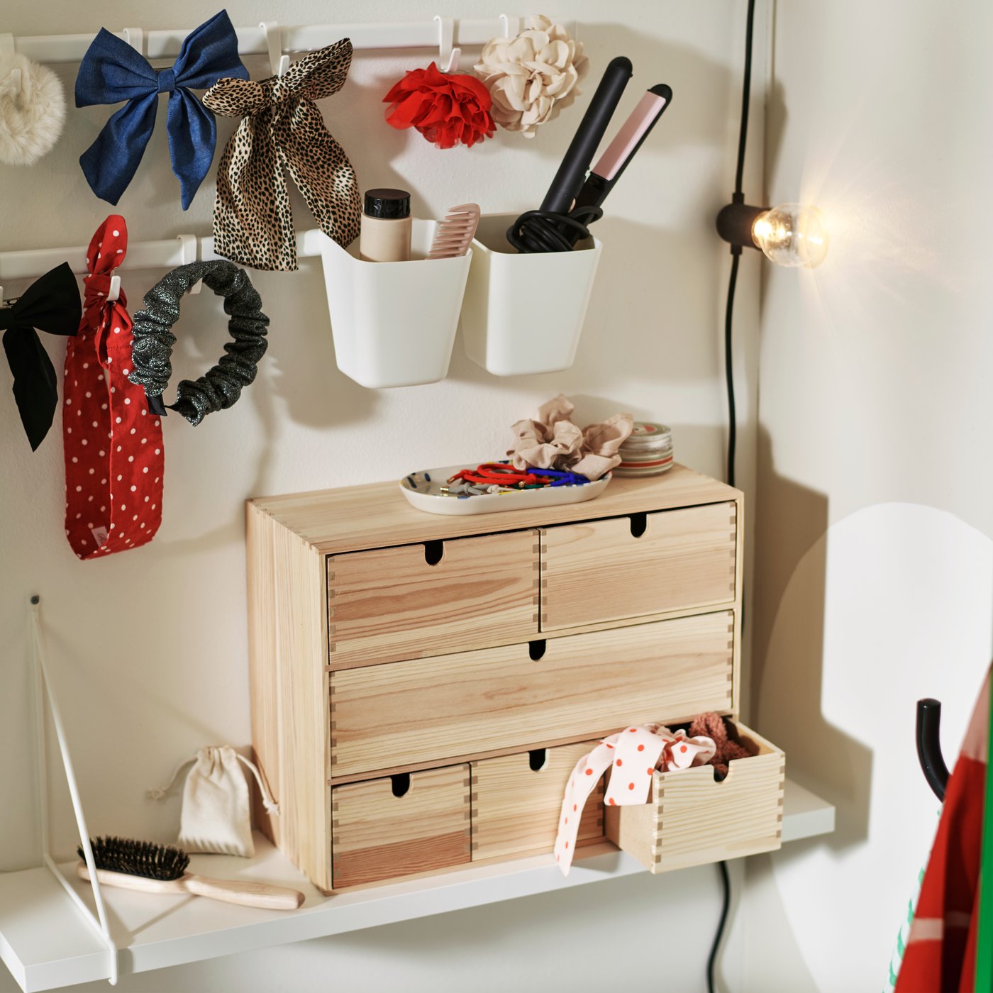 A MOPPE mini chest of drawers in light wood on top of a white shelf holds hair accessorises, with two hook rails above it.