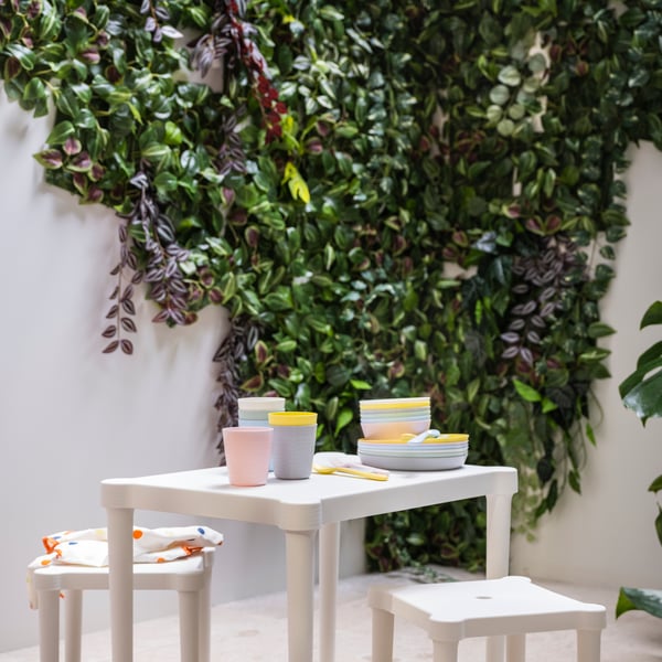 A collection of colourful KALAS mugs arranged on a white table, surrounded by greenery and soft natural light.