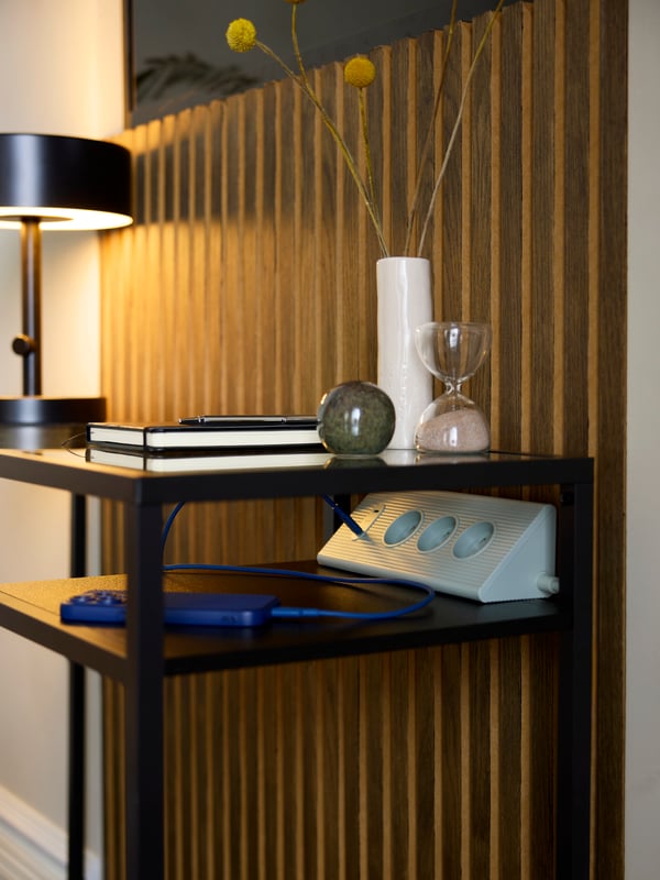 A triangular-prism shaped SKOTAT green extension cord has a phone plugged into its USB-C port, on a hotel room’s desk.