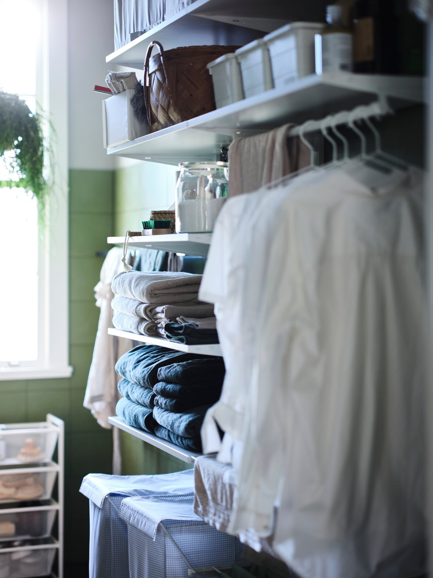 A white BOAXEL laundry combination with white shirts hanging from the rail, folded clothing on open shelves, and boxes above.