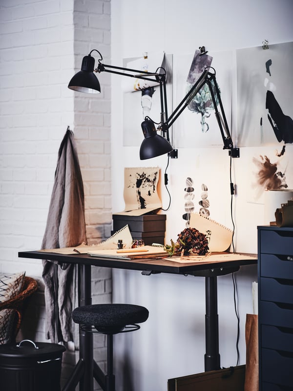 An IDÅSEN sit/stand desk covered in illustrated pages with a LIDKULLEN active sit/stand support.