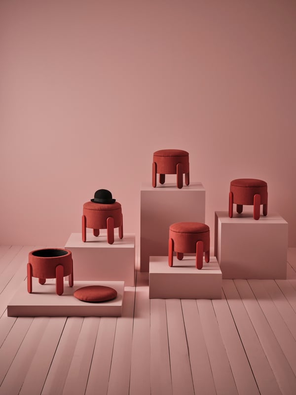 Five red FÖRLUNDA pouffes with storage are shown in a pink room. One pouffe is open and another has a black hat on top.
