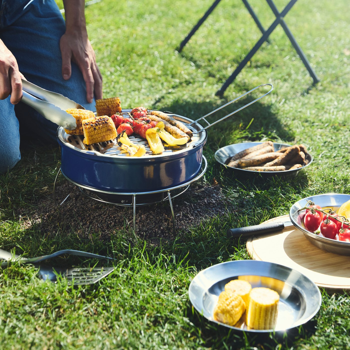 Barbecuing vegetables in the park on a blue STRANDÖN portable barbecue.